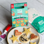Cookie decorating kit with heart and star-shaped cookies, icing tube, and packaging on a wooden table.