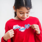 Girl in red shirt looking at London-themed stickers on her chest, including "I Love London" and a Union Jack heart.