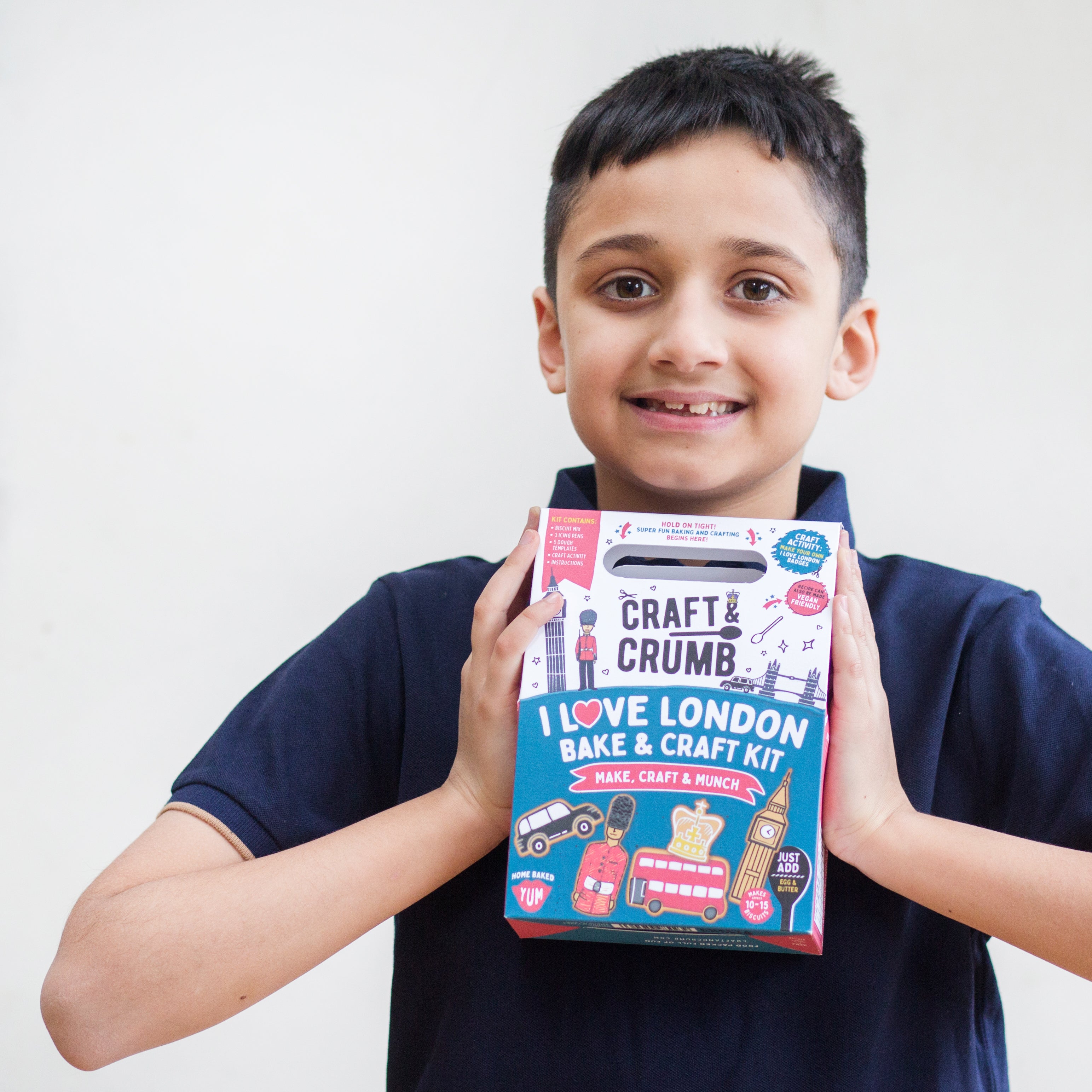 Boy holding a "Craft & Crumb" London-themed bake and craft kit, smiling at the camera.
