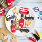 Cookies shaped like London icons: guards, buses, taxis, Big Ben, and crowns on a white plate.