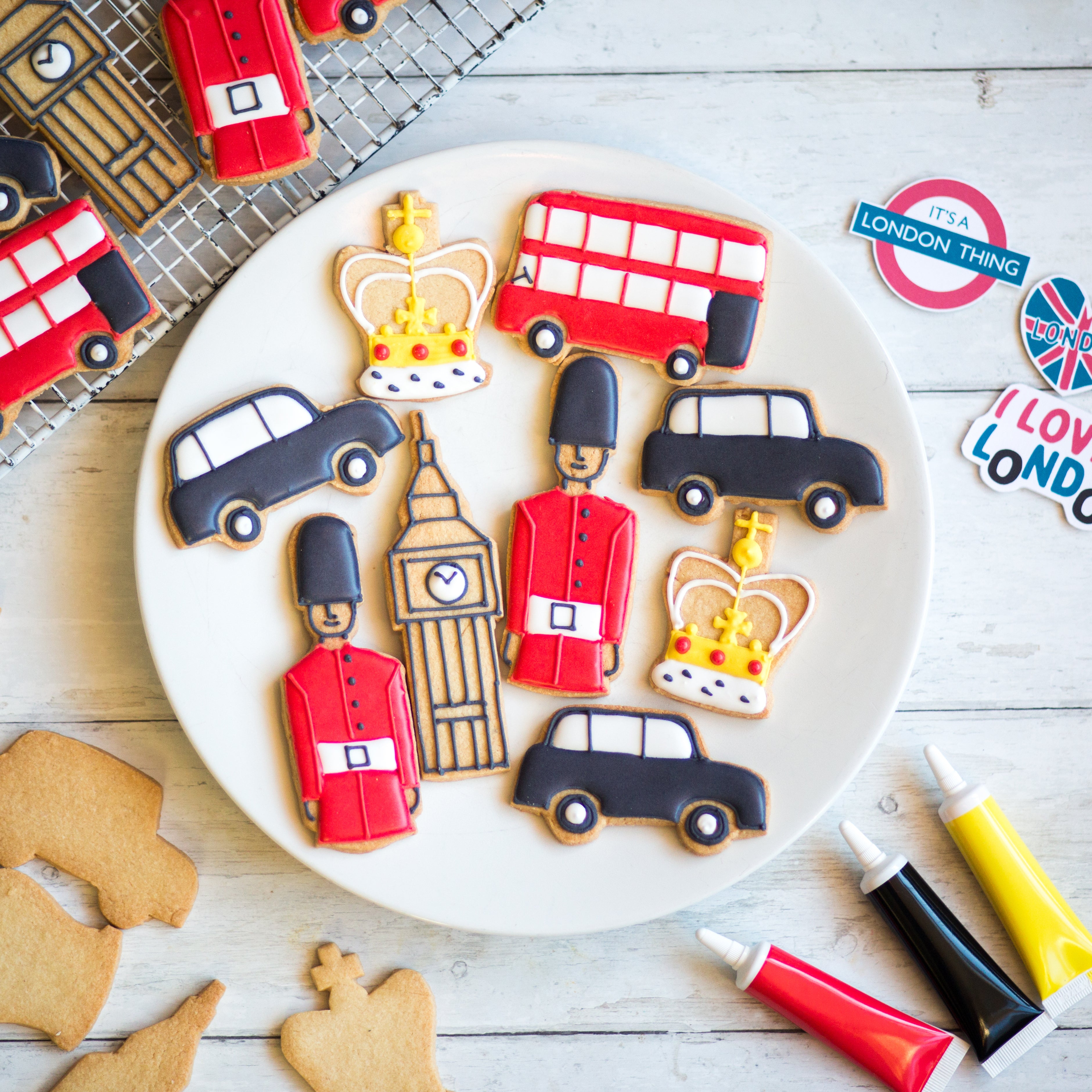 Cookies shaped like London icons: guards, buses, taxis, Big Ben, and crowns on a white plate.