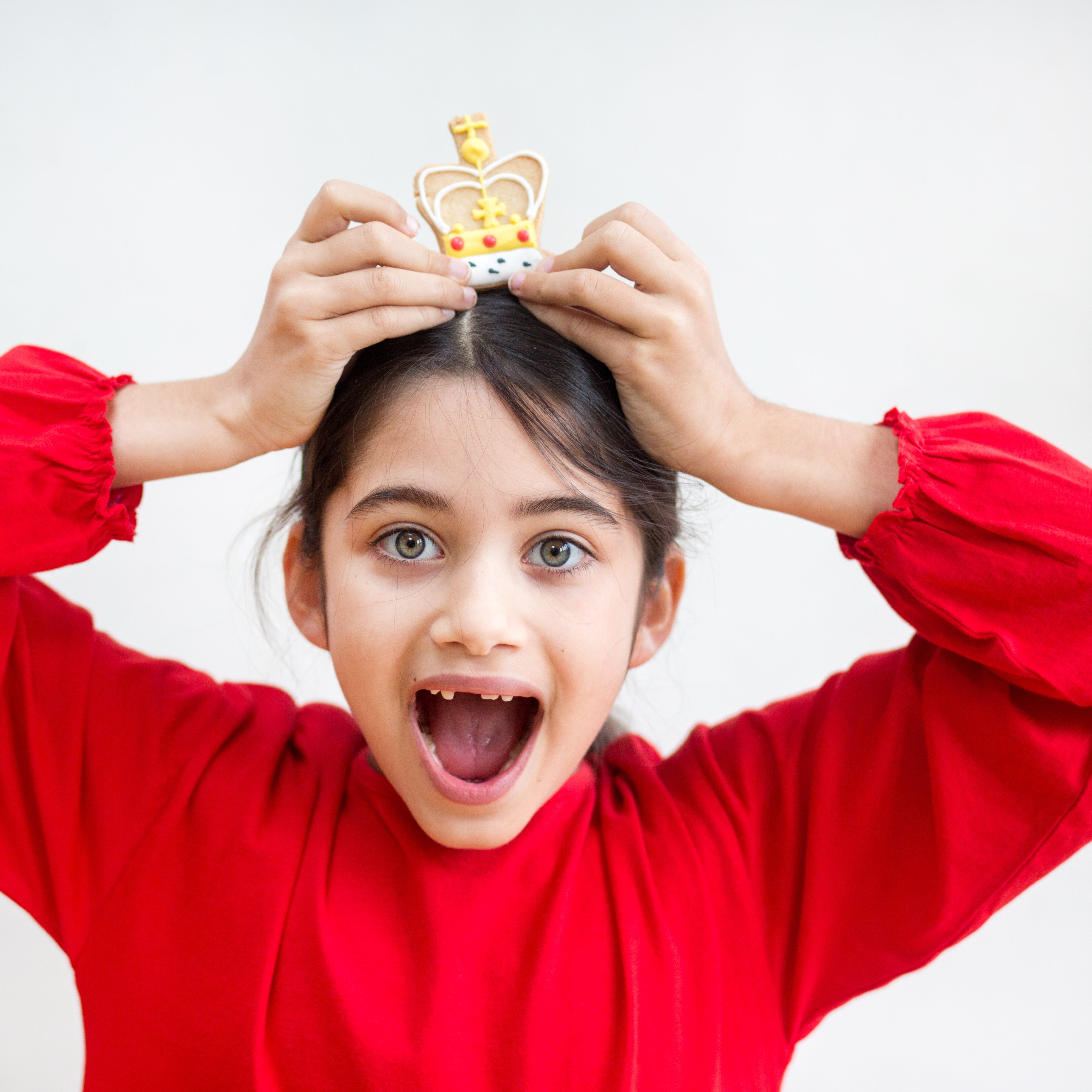 Child in red shirt holding a small crown above their head, with an excited expression.