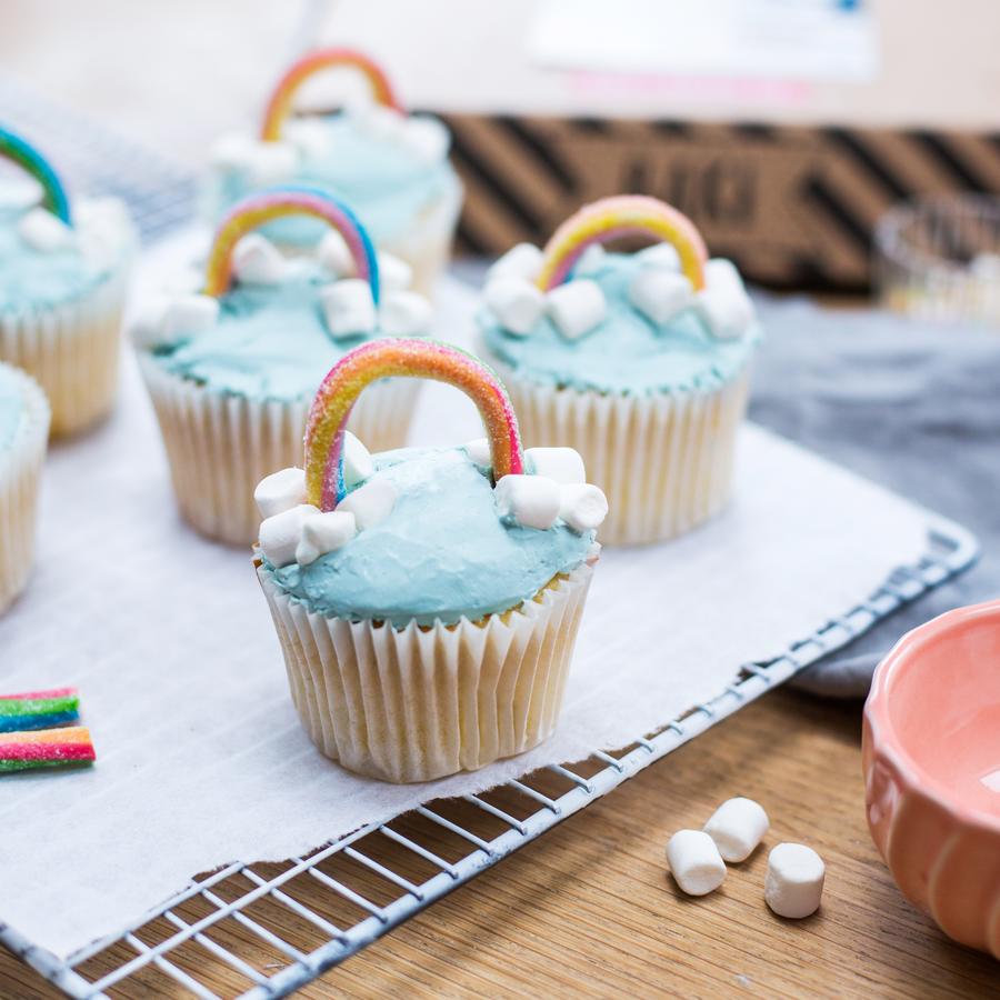 Colorful rainbow cupcakes with blue frosting and marshmallows on a cooling rack, from Craft & Crumb's kids baking kits.