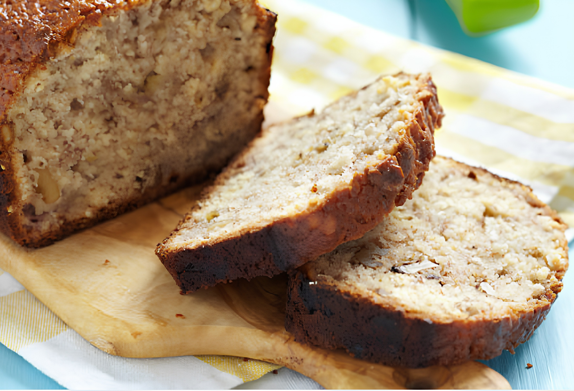 A close-up shot of a loaf of freshly baked banana bread on a wooden cutting board, with two thick slices cut and overlapping in the foreground.