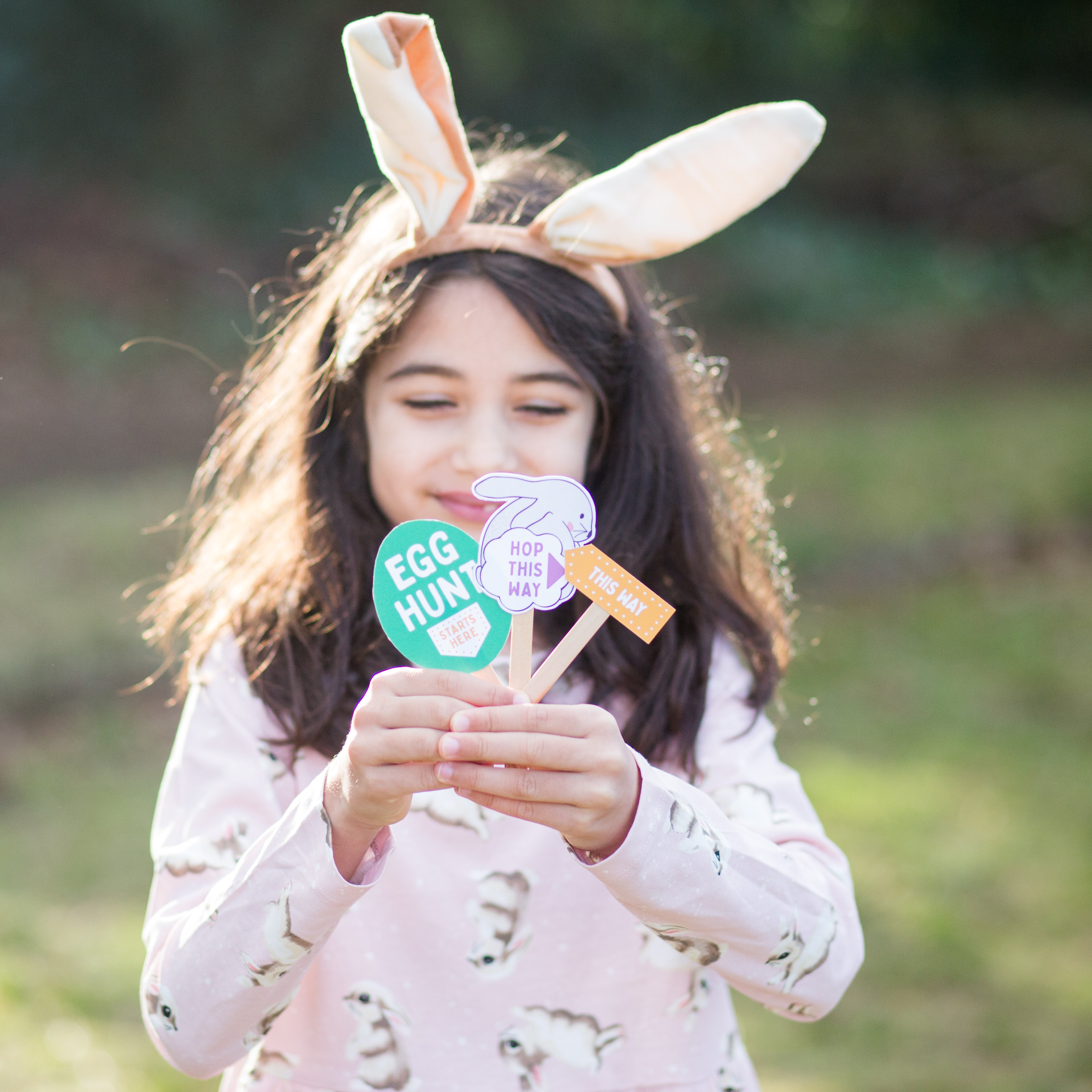 Girl with bunny ears holding Easter-themed signs outdoors.