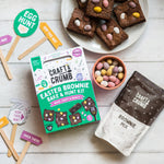 Easter brownie kit with mix, decorated brownies, mini eggs, and festive props on a white surface.