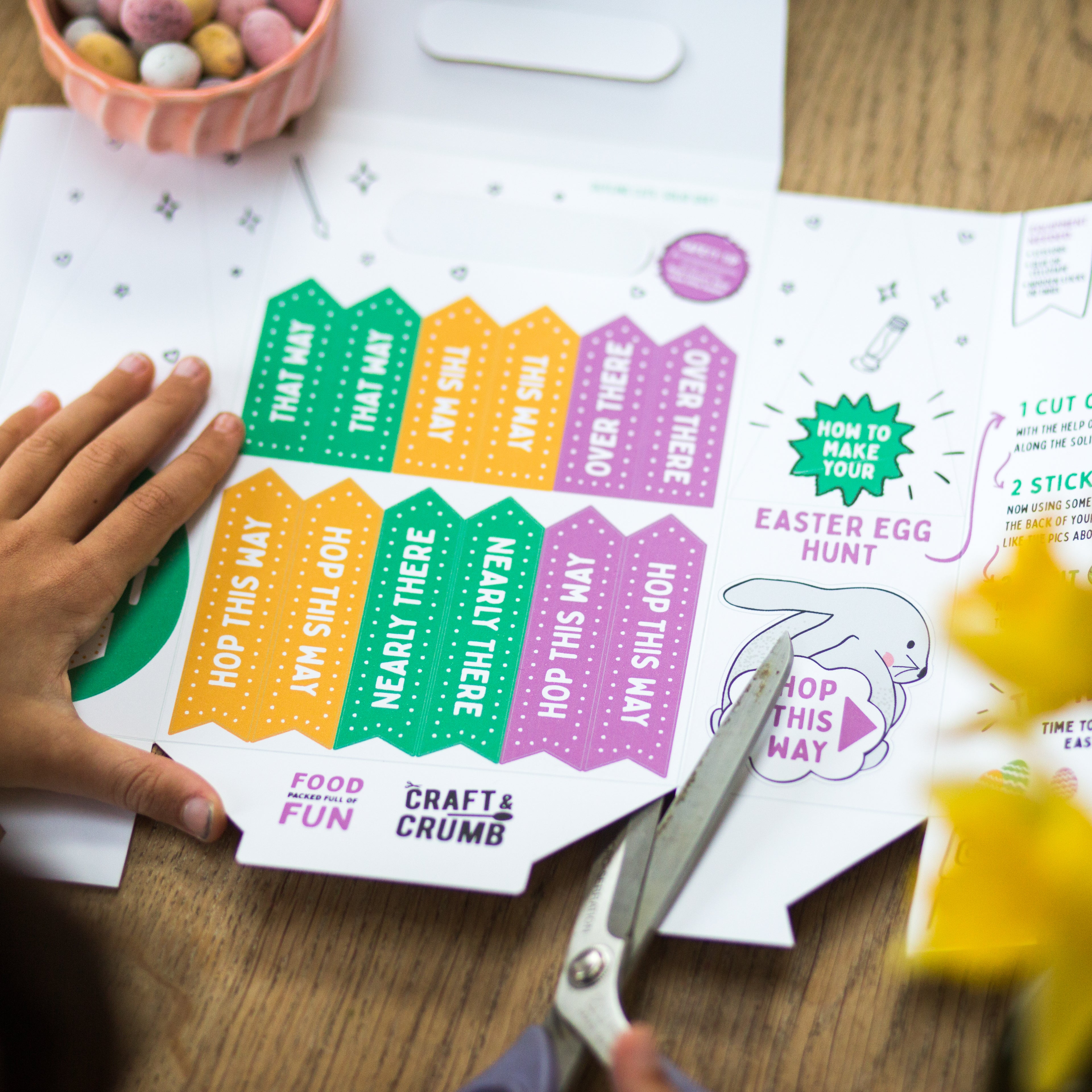 Person cutting colorful Easter egg hunt signs with scissors.