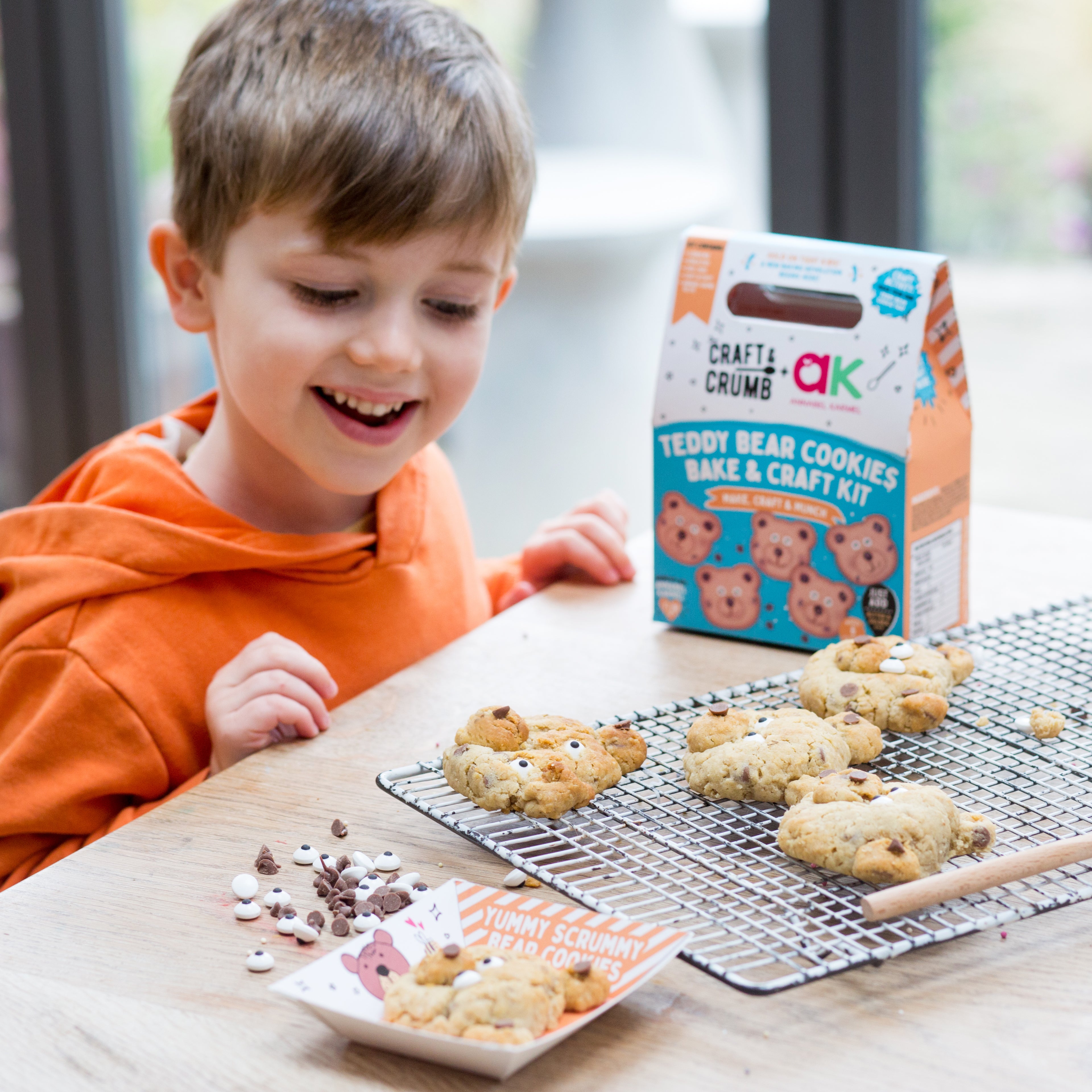 Child smiling at teddy bear-shaped cookies on a cooling rack, with a cookie kit box nearby.