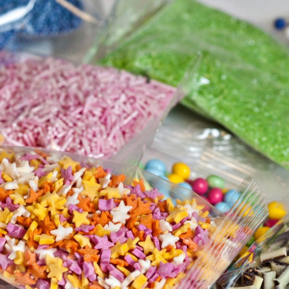 Colorful star-shaped sprinkles and various decorative toppings in clear bags on a table.