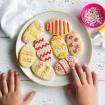 Plate of decorated Easter egg cookies with colorful icing and sprinkles, surrounded by a child's hands.
