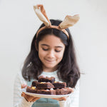 Girl with bunny ears holding a plate of brownies, smiling softly.