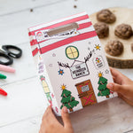 Child decorating a festive box with reindeer and Christmas tree designs, cookies and markers on a white table.
