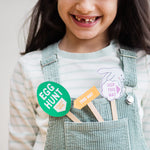 Smiling child in striped shirt and overalls holding Easter-themed signs with phrases like "Egg Hunt" and "Hop This Way."