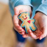Child holding a small teddy bear-shaped cookie with blue icing and a red heart.