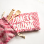 Red striped pouch with wooden spoon and stamper, next to a matching cloth with "Craft & Crumb" text.