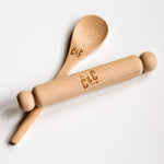 Wooden rolling pin and spoon with "C&C" logo engraved, placed on a white surface.