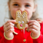 Child holding a reindeer-shaped cookie with icing details, wearing a red sweater.