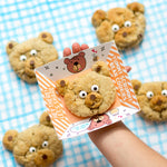 Child holding a bear-shaped cookie on a card, surrounded by more cookies on a blue checkered cloth.