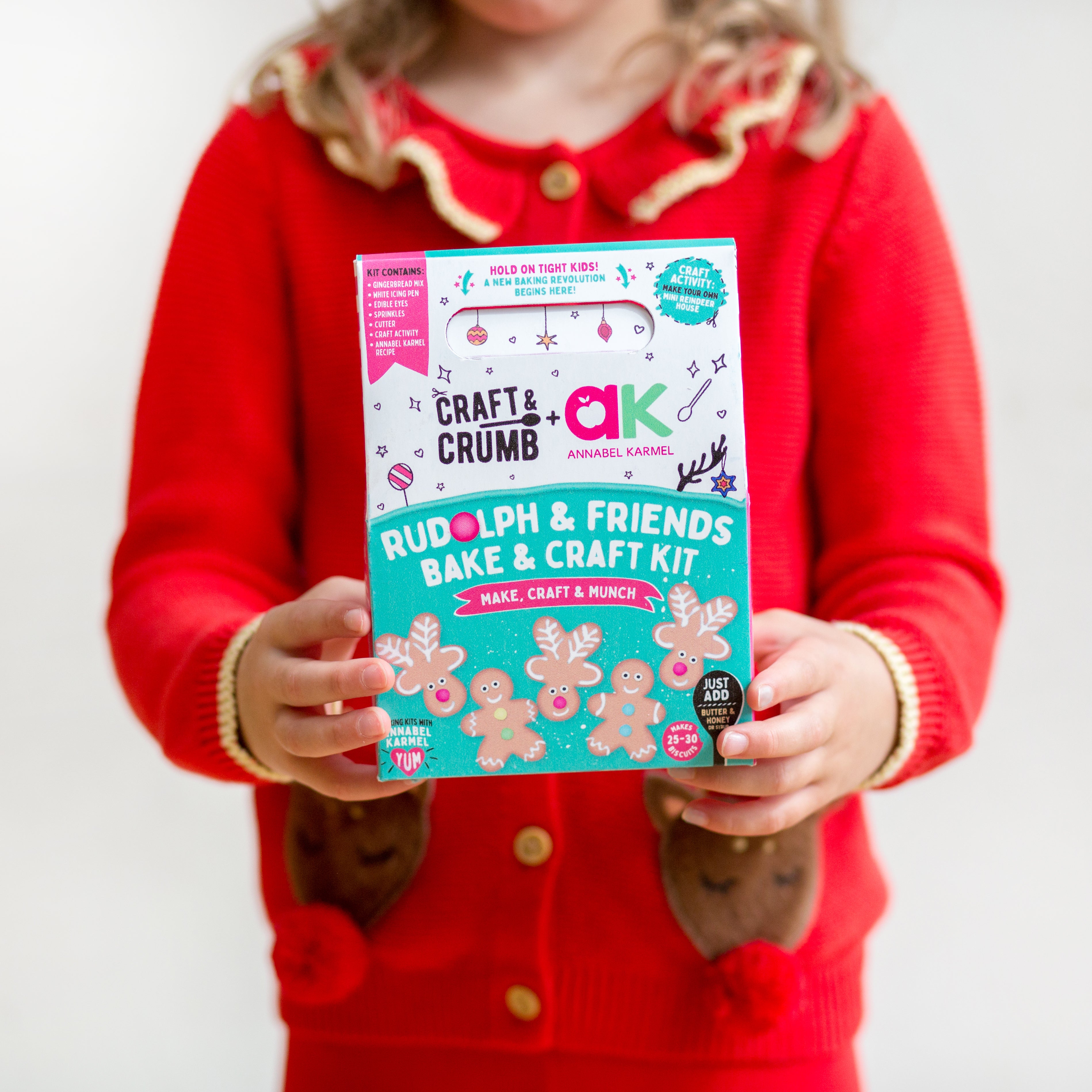 Child holding a "Rudolph & Friends Bake & Craft Kit" in a festive red outfit.