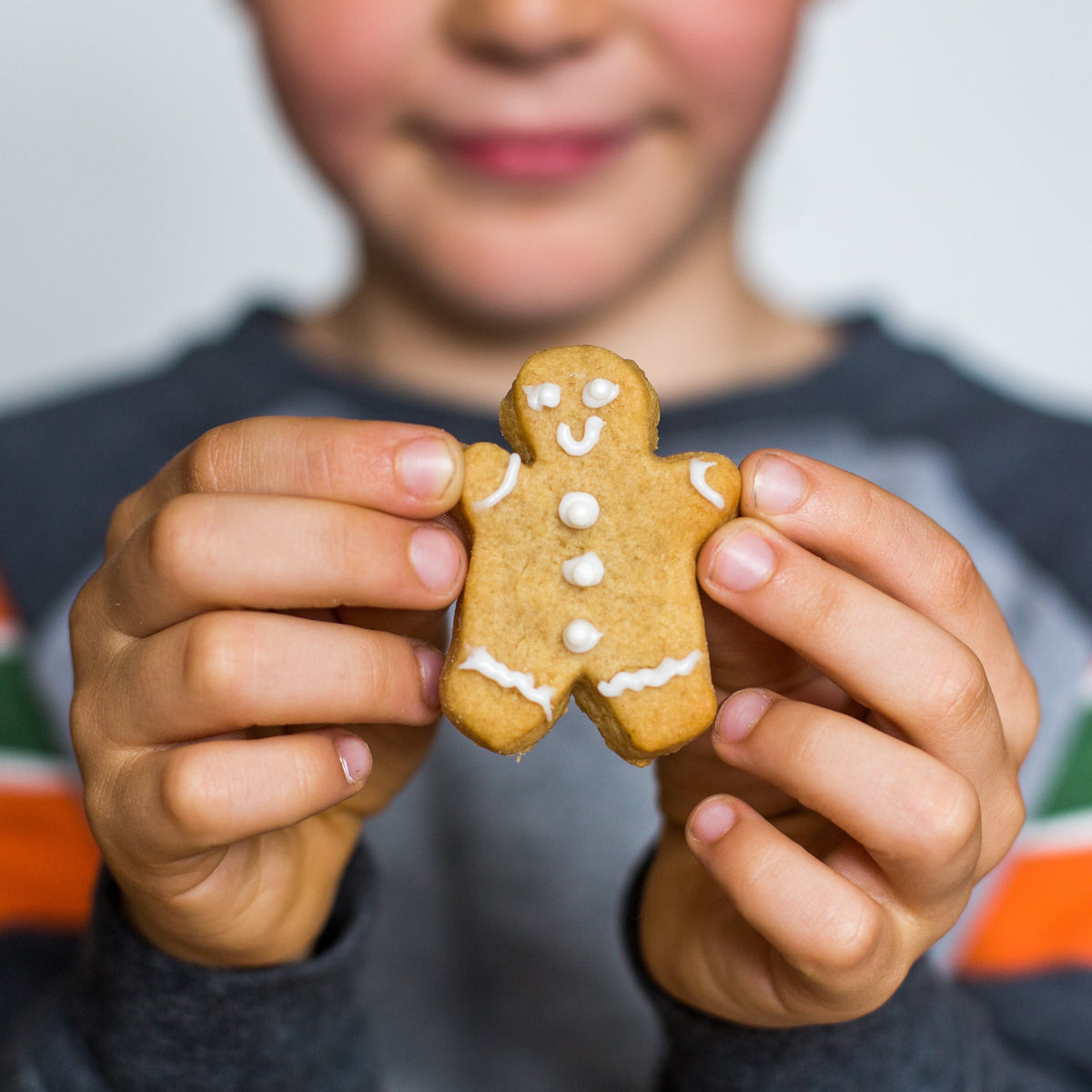 Child holding a decorated gingerbread man cookie with icing details, smiling face, and buttons.