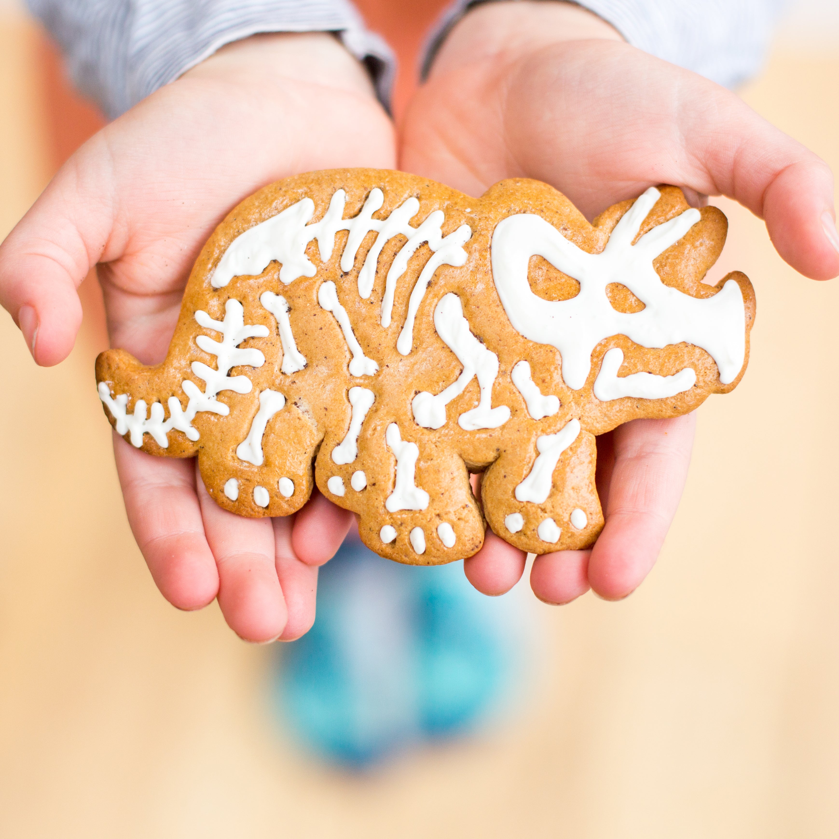 Hands holding a dinosaur-shaped cookie with white icing resembling a skeleton.