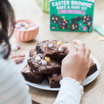 Person decorating brownies with mini eggs, Easter brownie kit box in background.