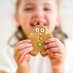 Child holding a gingerbread cookie with icing eyes and buttons, smiling in the background.
