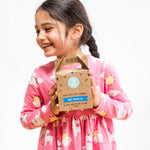 Smiling girl in pink dress holding a party pancake kit box against a white background.