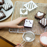 Child decorating brownies with powdered sugar using stencils on a cooling rack.