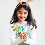Girl with bunny ears holding Easter egg hunt signs, smiling.