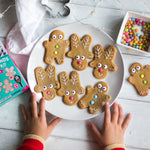 Child's hands reaching for a plate of decorated reindeer and gingerbread cookies with colorful candies on a wooden table.