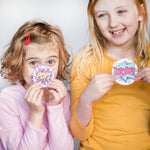 Two children smiling, holding comic-style signs reading "POP!" and "WOW!" against a light background.