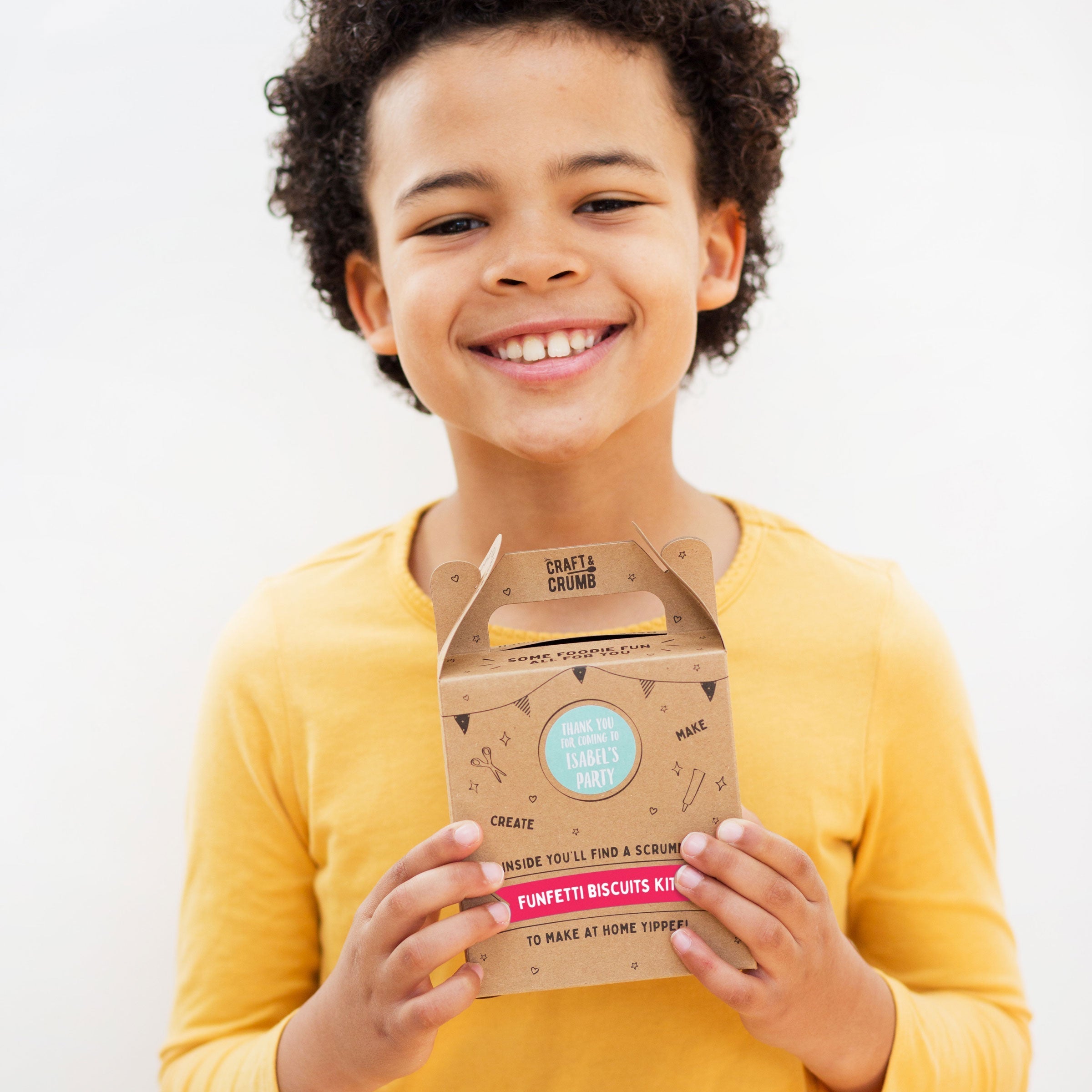 Child smiling and holding a "Funfetti Biscuits Kit" box, wearing a yellow shirt against a plain background.