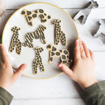 Child's hands holding a plate of safari animal cookies, including leopard, zebra, and giraffe designs.