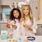 Woman and child with bunny ears decorating Easter biscuits in a kitchen.