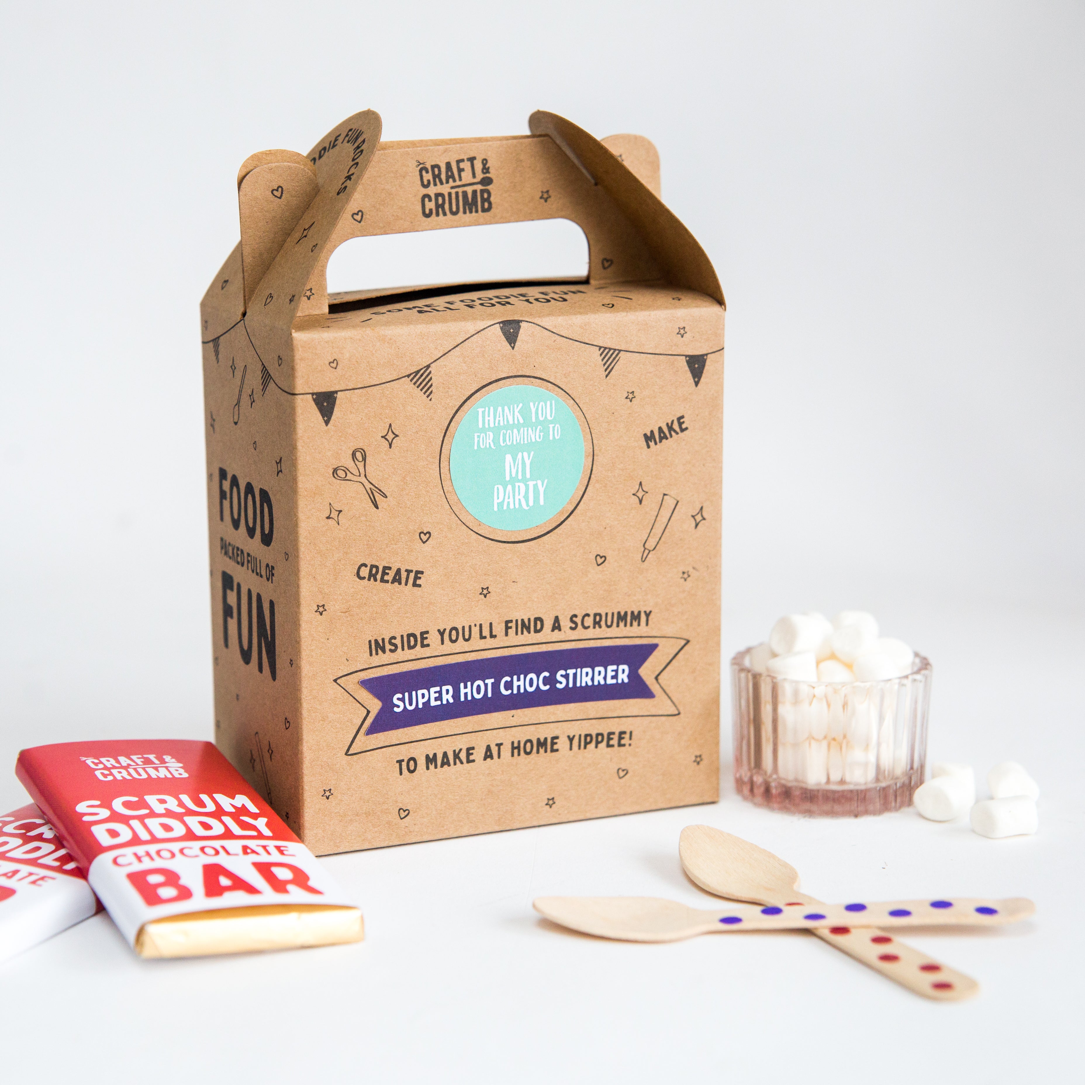 Craft & Crumb party box with hot chocolate stirrer, chocolate bars, wooden spoons, and marshmallows on a white background.