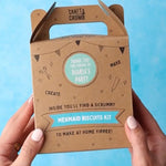 Hands holding a brown box labeled "Mermaid Biscuits Kit" against a blue background.