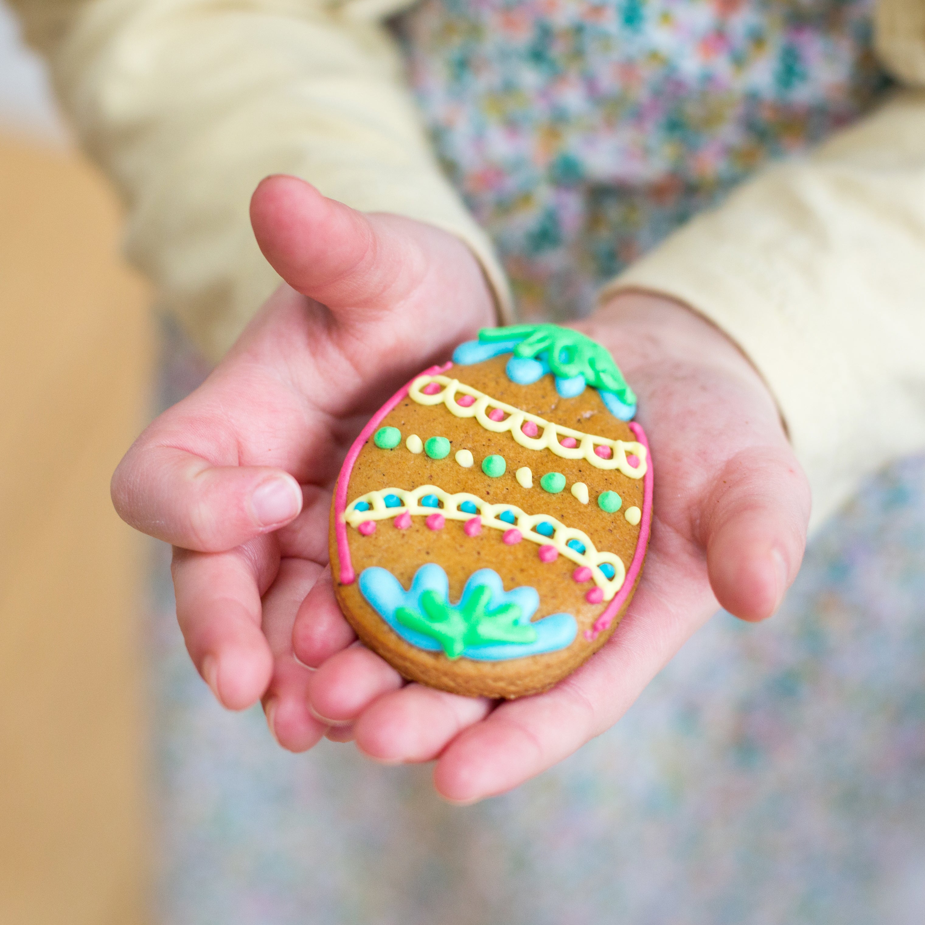 Child holding an Easter egg-shaped cookie decorated with colorful icing patterns.