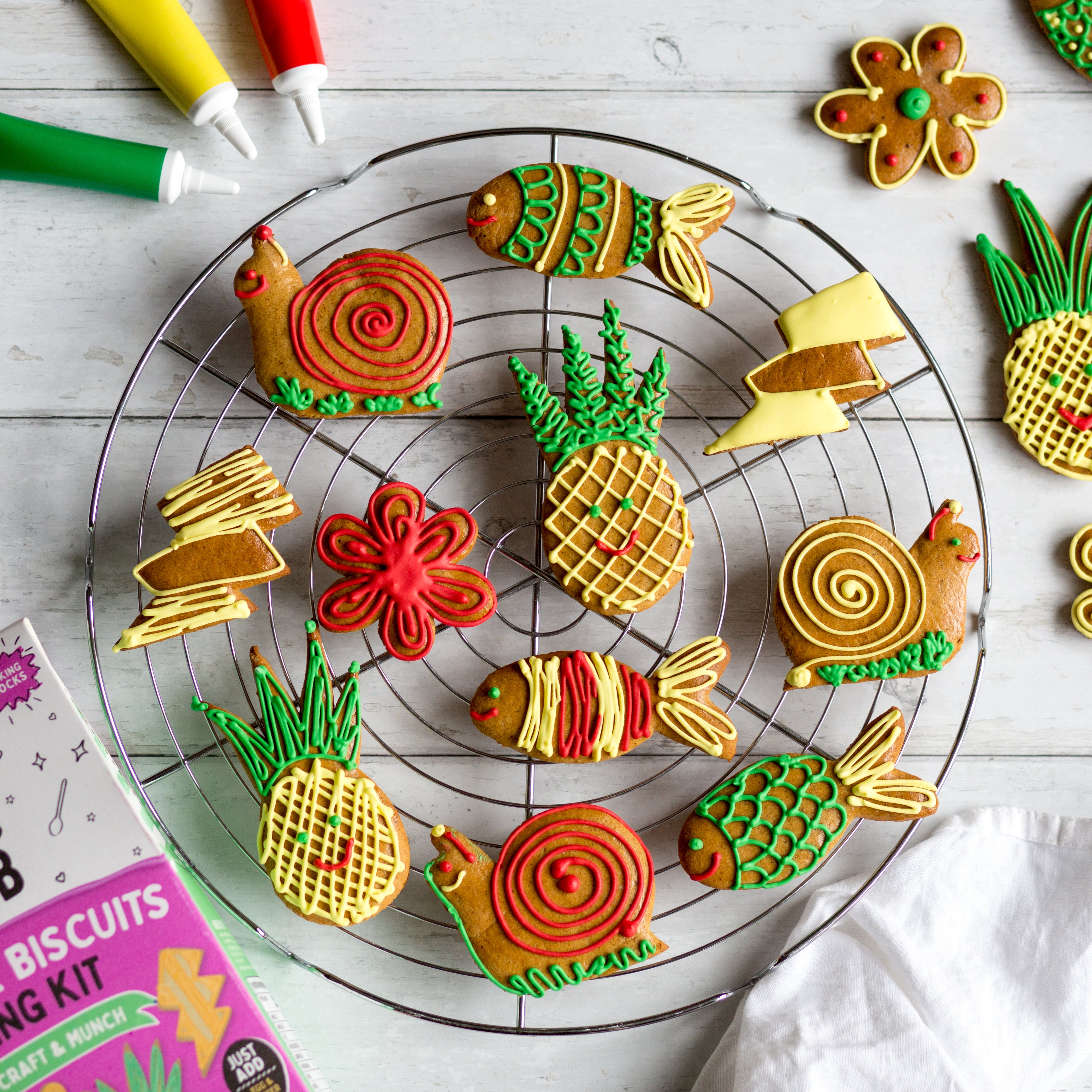 Colorful animal and fruit-shaped cookies on a cooling rack, with icing tubes and a decorating kit nearby.