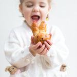 Child holding a bunny-shaped bread roll, smiling with excitement, wearing a white sweater with small animal pockets.