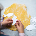 Child holding a paper lightning bolt over rolled dough, surrounded by paper shapes on a gray surface.