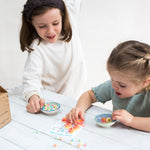Two young girls playing a game with colorful cereal pieces on a table, smiling and engaged.
